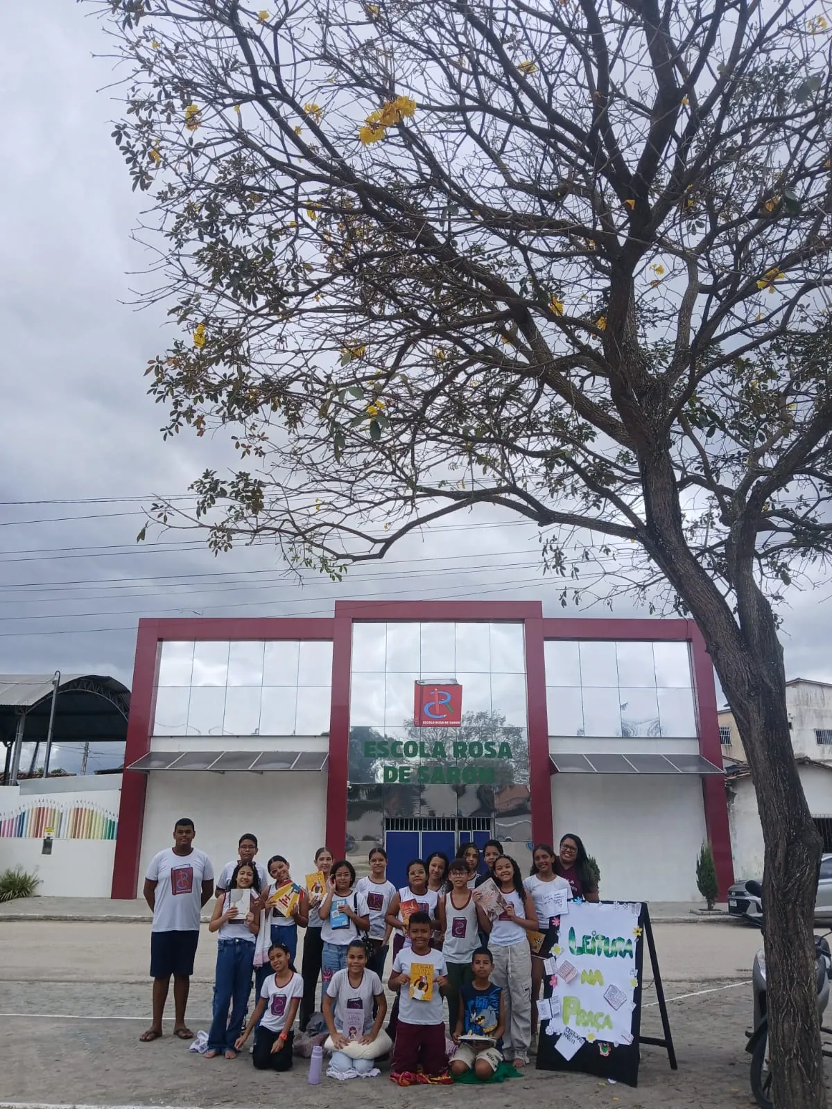 Alunos posando com livros em frente à fachada da escola durante o Leitura na Praça